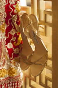 Gold bridal Jimmy Choos hanging up through trellis next to red and gold bridal dress