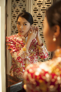 Bride is red and gold Chinese dress putting her earrings on