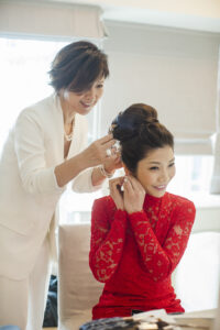 Woman in red outfit with hairdresser in whte fixing the Bridal hair