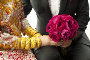 Bride with lots of gold bangles and groom holding hands with pink rose bouquet