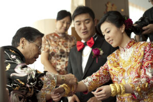 Family member adding bangles to Chinese bride