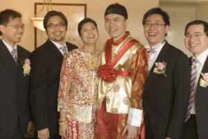 Bride and groom with groomsmen smiling. Bride and groom are wearing traditional red and gold Chinese wedding attire