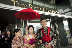 Bride, groom and family exiting The Ritz Carlton following a traditional Chinese Tea Ceremony with a red umbrella held above them