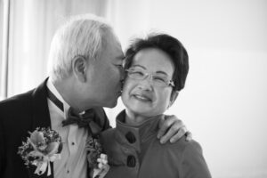 Black and white photo of older male gentleman giving his wife a kiss on the cheek