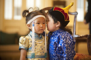 Young girl and boy whispering to each other wearing blue and gold Chinese outfits