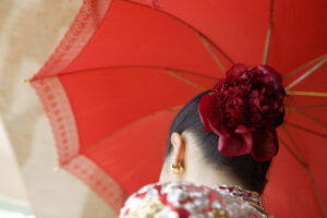 Chinese bride holding red umbrella with beautiful red roses in her hair which is tied up in a bun