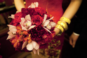 Woman holding a red and pink floral bouquet wearing gold bangles