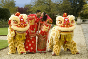 Bride and groom holding red and gold traditional Chinese banners, kissing, between two gold Chinese dragons