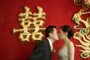 Bride and groom kissing in front of a red background with gold chinese writing