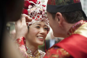 Bride wearing a traditional headdress with groom brushing some decoration from her face