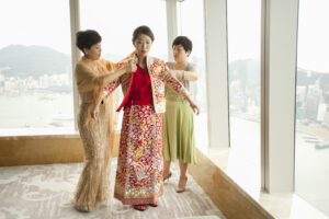 Bride being dressed into Chinese bridal gown by 2 female family members