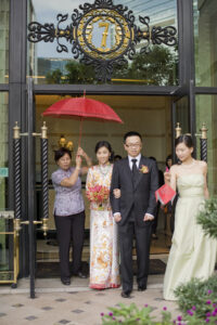 Bride and groom leaving The Ritz Carlton under a red umbrella with a bridesmaid