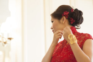 Bride in red Chinese dress putting on earrings